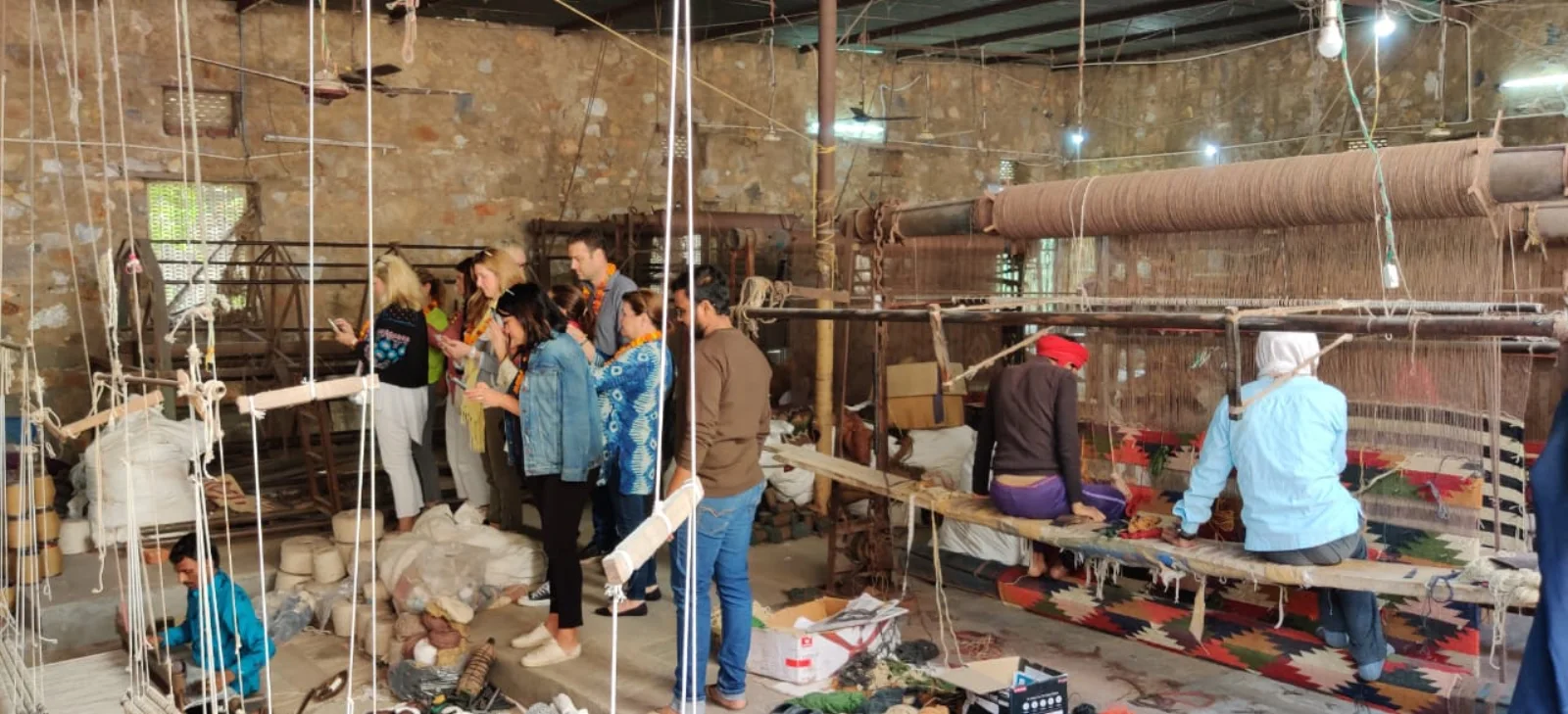 Visitors observing artisans weaving rugs on workshop looms
